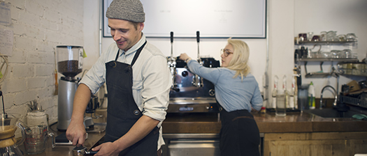 A cafe setting with two staff wearing aprons who are making coffee