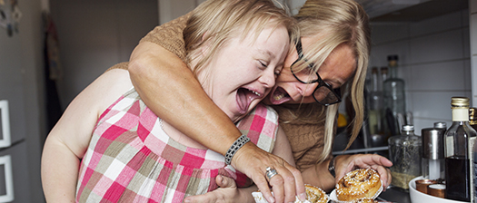 A mum and her daughter with disability laughing while cooking in the kitchen
