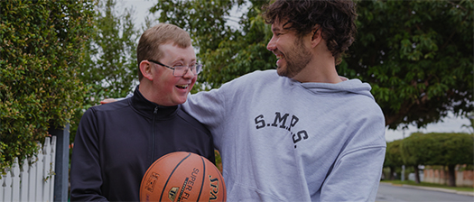 Two males with a basketball smile at each other.